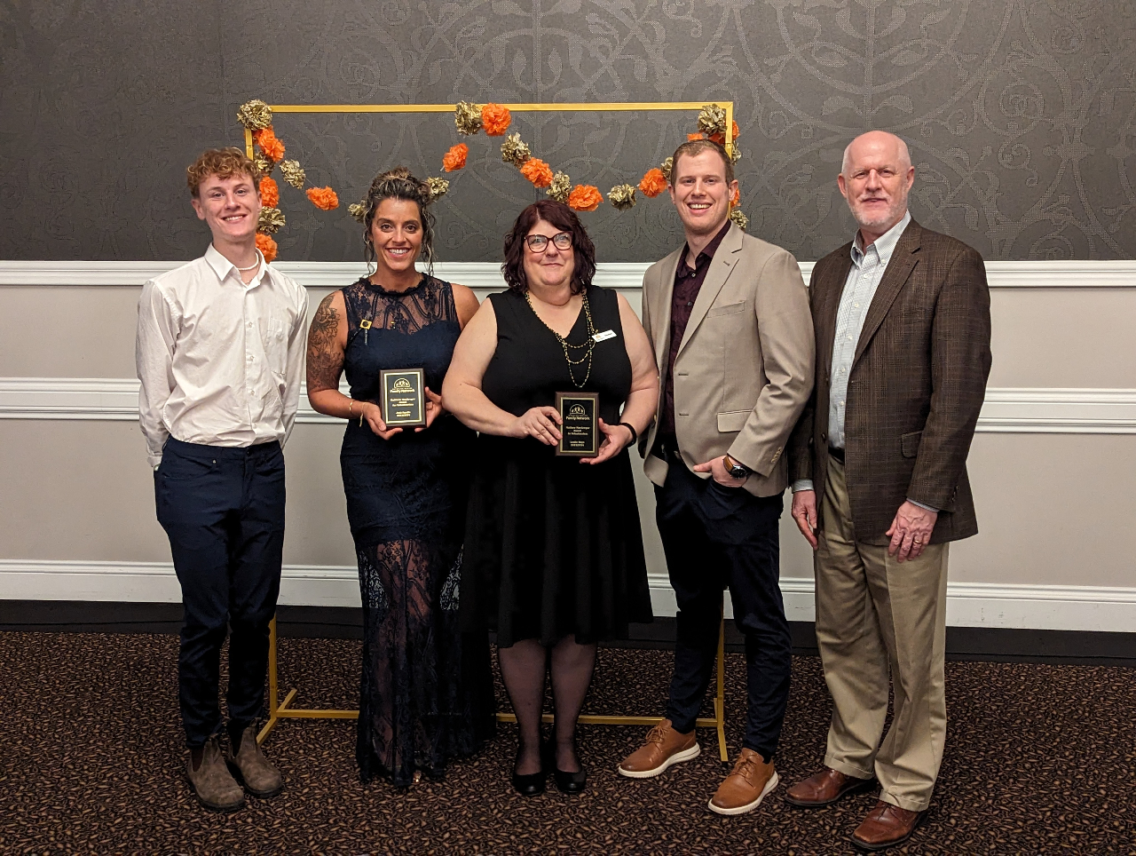 This photo features the Matthew McGregor Volunteer Award winners, Jodi and Leslie, posing and smiling with the McGregor family. All parties are dressed in formal attire, dark dresses and lighter-coloured suits.